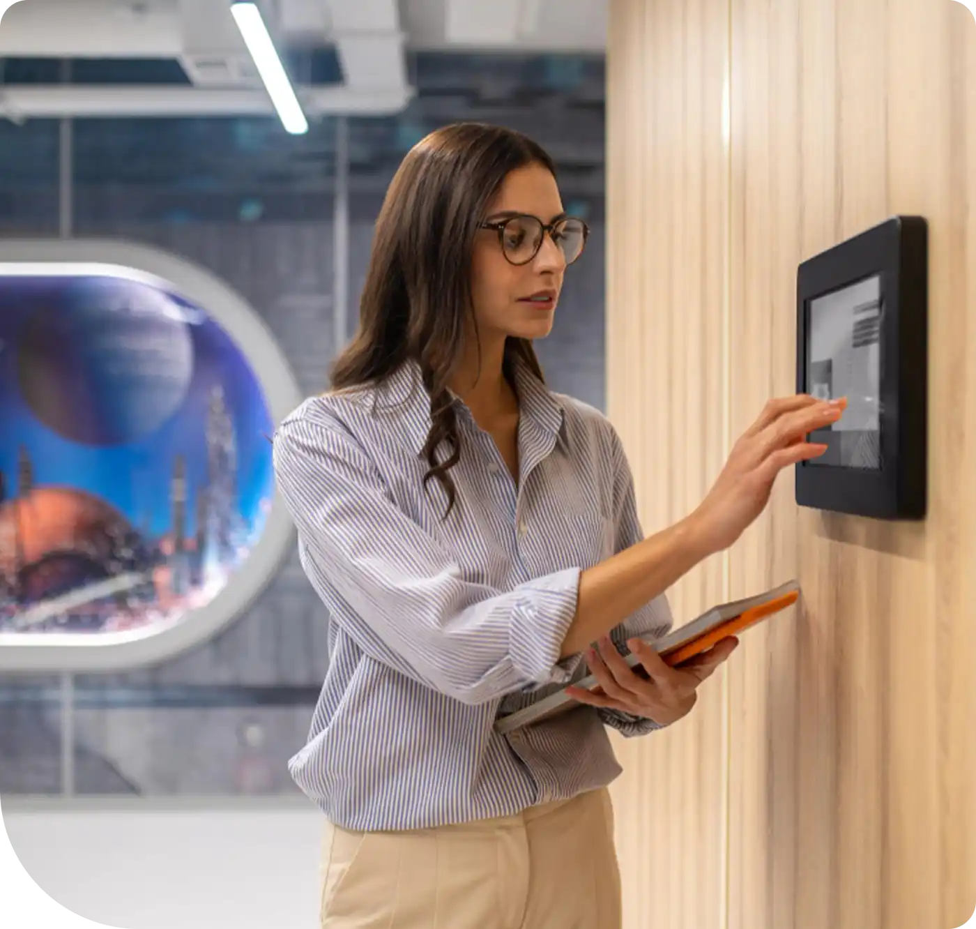 A woman interacting with a wall-mounted touch panel in an office setting